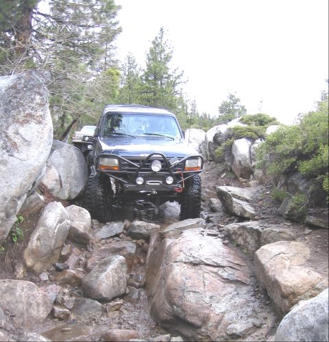 1994 Ford Bronco - A modified Ford Bronco drives through a challenging rocky terrain on an off-road trail.