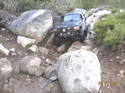 1994 Ford Bronco - A dark blue 1994 Ford Bronco navigates a challenging rocky trail, with another vehicle visible behind it.