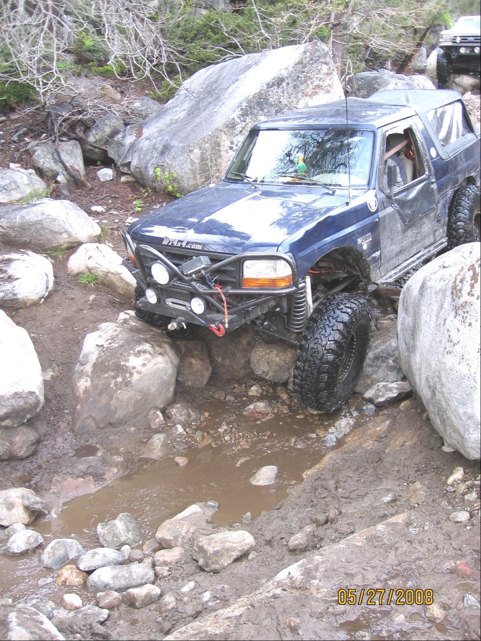 Blue Ford Bronco with soft top and winch bumper crawling down rocky creek bed
