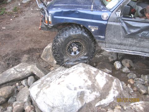 1994 Ford Bronco - A blue 1994 Ford Bronco navigates a rocky trail, with one tire deflated.