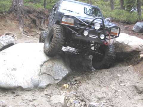1994 Ford Bronco - Modified 1994 Ford Bronco tackling a challenging off-road obstacle with large tires.