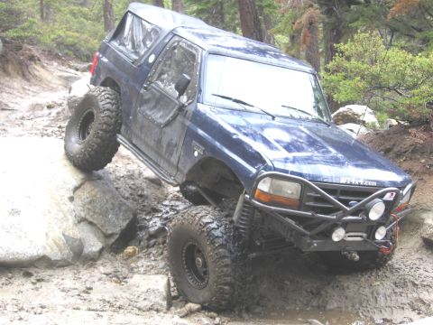 1994 Ford Bronco - This modified SUV is shown tackling a challenging off-road course with steep inclines and obstacles.