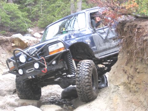 1994 Ford Bronco - A modified blue SUV tackles a challenging off-road trail with steep inclines and large rocks.