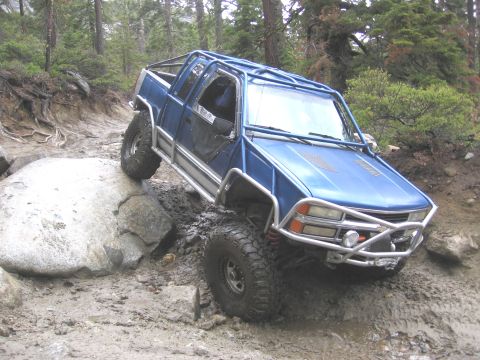 1994 Ford Bronco - This heavily modified blue truck, equipped with a full roll cage and off-road tires, tackles a challenging rocky and muddy terrain.