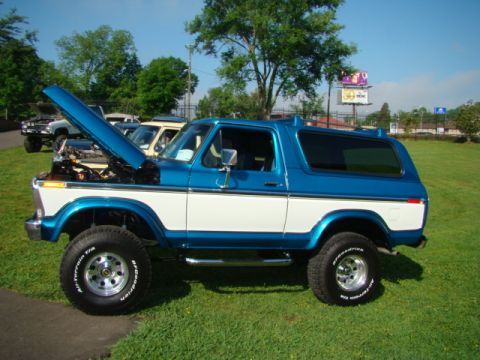 1994 Ford Bronco - Side view of a two-tone blue and white Ford Bronco, hood up, parked outdoors with other vehicles nearby.