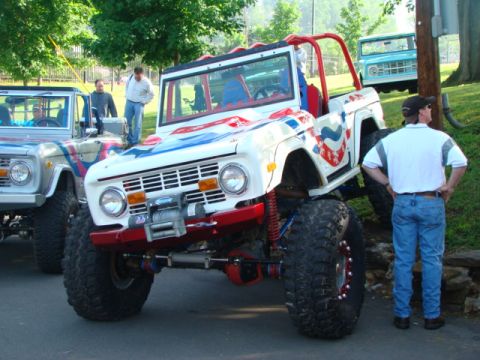 1994 Ford Bronco - A heavily modified Bronco with custom paint sits parked next to another Bronco, with a third in the background.