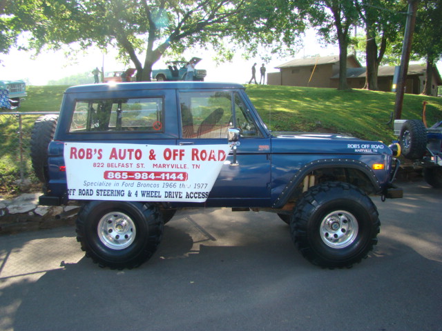 Blue Ford Bronco with large tires and "ROB'S AUTO & OFF ROAD" banner specializing in 1966-1977 Broncos