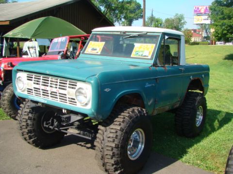 1994 Ford Bronco - This lifted Ford Bronco features large off-road tires and a white hardtop. Two yellow signs are visible on the windshield.