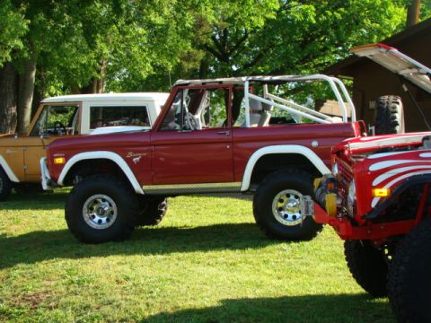 1994 Ford Bronco - Several Ford Broncos are parked on a grassy lawn under trees, with one having its hood open.