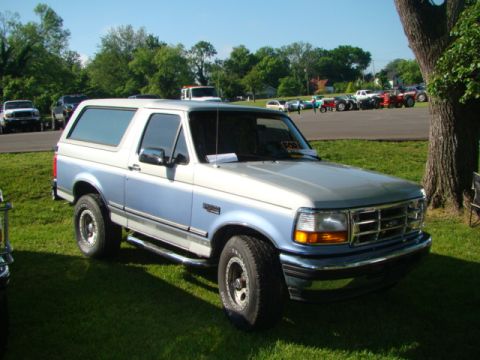 1994 Ford Bronco - This two-tone blue and silver 1994 Ford Bronco is parked on a grassy lawn with other vehicles in the background.