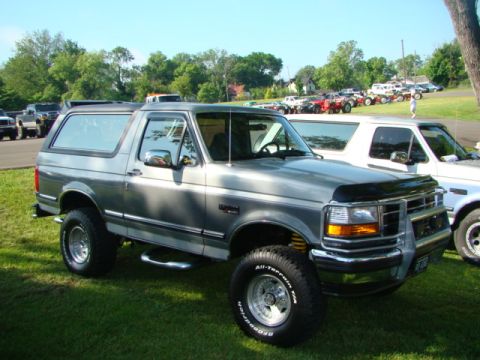1994 Ford Bronco - A lifted silver-gray full-size Ford Bronco SUV parked on grass at an outdoor car show, viewed from the three-quarter front. It wears a chro…