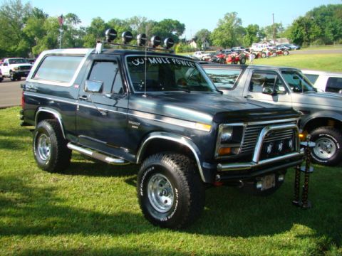 1994 Ford Bronco - A dark green/black full-size Ford Bronco SUV with a removable hardtop, shown from the front-three-quarter angle on grass at what appears to…