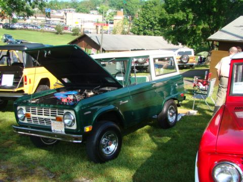 1994 Ford Bronco - A green Ford Bronco with its hood open is parked on a grassy field next to other vehicles.