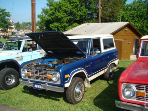 1994 Ford Bronco - A blue and white Ford Bronco is displayed with its hood open, alongside other Broncos at an outdoor event.