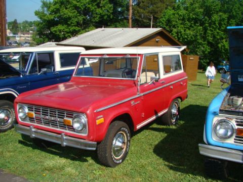 1994 Ford Bronco - A red Ford Bronco with a white top is parked on grass next to other vehicles.