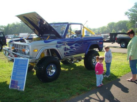 1994 Ford Bronco - This customized Ford Bronco features a flame paint job and an open hood, displayed with a descriptive sign.