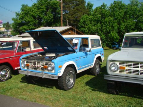 1994 Ford Bronco - Several Ford Broncos are parked on a grassy field with trees in the background.