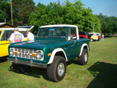 1994 Ford Bronco - A green Ford Bronco with a white top and fender flares is parked on a grassy field, with other vehicles visible in the background.