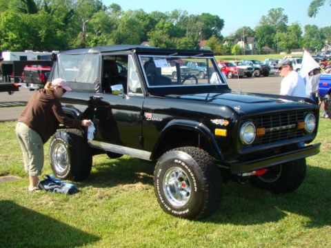 1994 Ford Bronco - A person polishes a black 1975 Ford Bronco convertible at an outdoor event with other vehicles in the background.