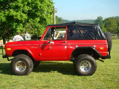 1994 Ford Bronco - A red 1978 Ford Bronco with a black soft top is parked on a grassy field under a clear sky.