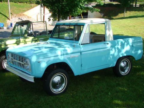 1994 Ford Bronco - Two Ford Broncos parked on grass, one light blue and one green, under trees.