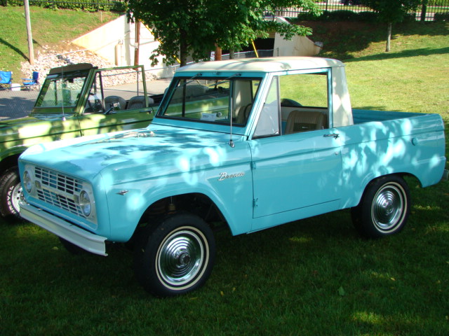 Light blue 1966-1977 Ford Bronco with white roof parked next to a green Bronco