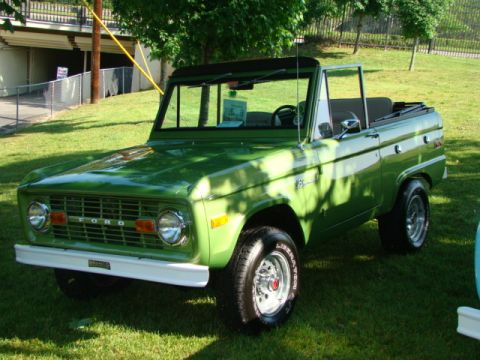 1994 Ford Bronco - A classic green Ford Bronco is displayed on a grassy area with trees in the background.