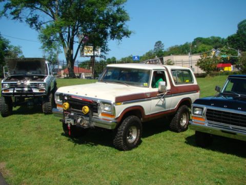 1994 Ford Bronco - This two-tone Bronco features a front winch and off-road tires, parked alongside other vehicles on a sunny day.