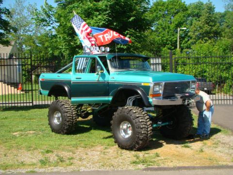 1994 Ford Bronco - A heavily modified pickup truck is parked on grass with flags flying from its roof.