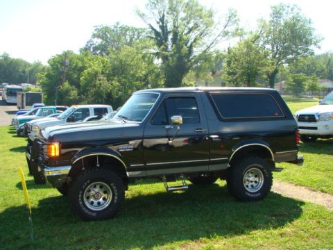 1994 Ford Bronco - A two-tone Ford Bronco is parked on a grassy field with other vehicles in the background.