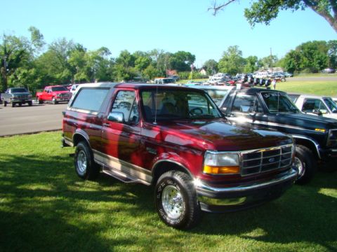 1994 Ford Bronco - A shiny red 1994 Ford Bronco is parked on the grass, with other vehicles in the background.