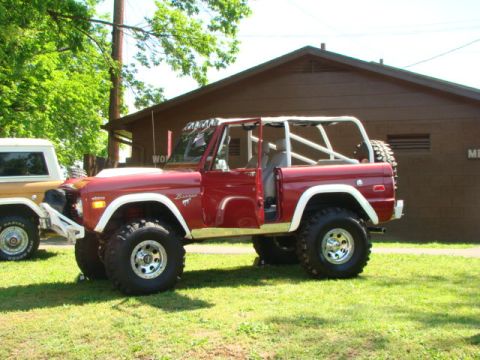 1994 Ford Bronco - Two Ford Broncos, one red and one tan, parked on a grassy area in front of a building.