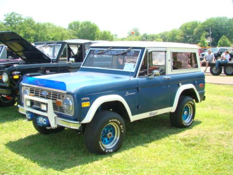1994 Ford Bronco - This classic blue and white Ford Bronco is parked on a grassy field next to other vehicles.