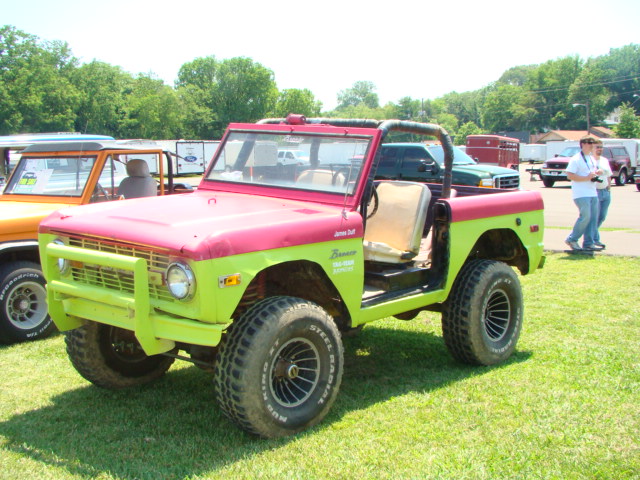 Two-tone red and lime green Ford Bronco with aftermarket bumper and roll cage. Another Bronco is parked to its left
