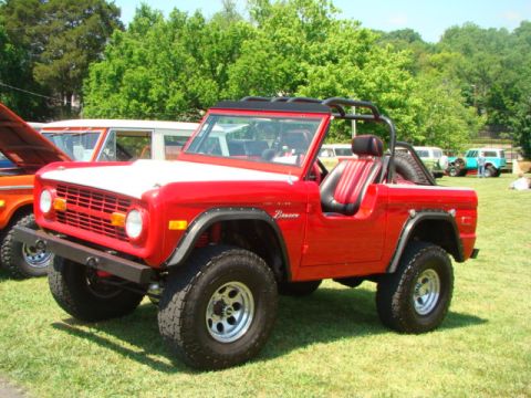 1994 Ford Bronco - A red Ford Bronco is parked on grass with other vehicles in the background at an outdoor event.