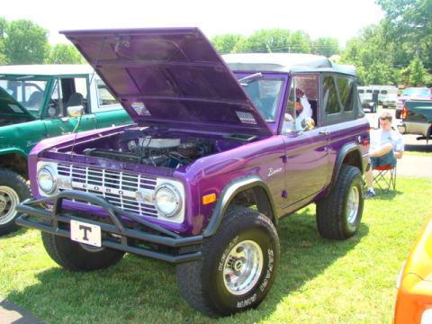 1994 Ford Bronco - A purple Ford Bronco is displayed with its hood open, parked next to another Bronco.