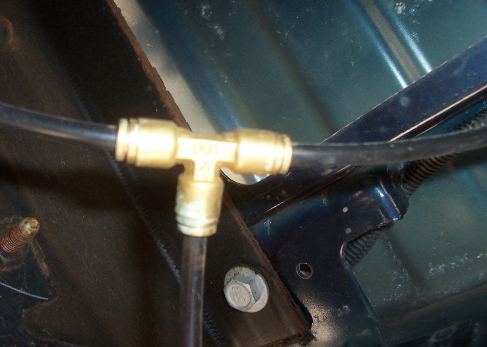 Close-up of a brass tee fitting connecting black air lines under a vehicle