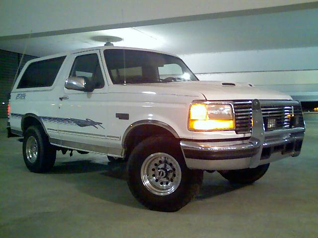 White 1996 Ford Bronco with a chrome bull bar and aftermarket wheels parked in a garage