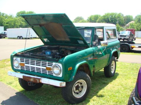1994 Ford Bronco - A classic green Ford Bronco from the early 1970s is displayed with its hood raised, revealing the engine compartment.