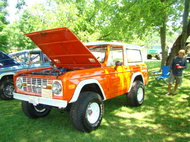 Orange Ford Bronco with hood open, parked next to a blue vehicle on grass