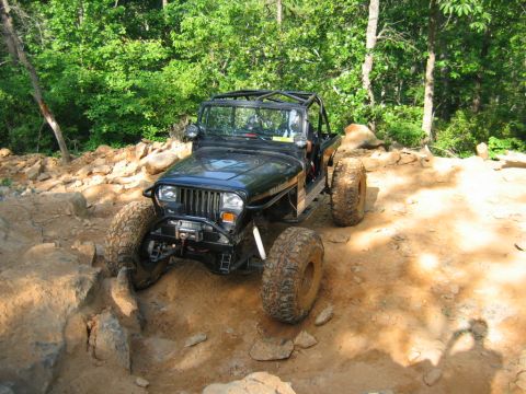 1992 Ford Mustang - A modified Jeep navigates a challenging off-road course with steep inclines and large rocks.