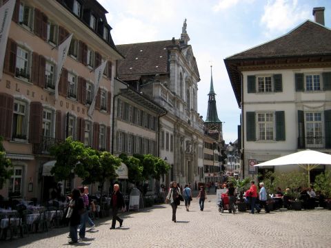1996 Ford Bronco - A bustling European town square with historic buildings, outdoor seating, and pedestrians enjoying the day.