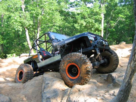 1992 Ford Mustang - Modified black Jeep Wrangler navigates a challenging rocky trail with its large, aggressive tires.