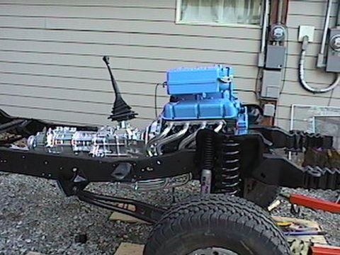 1992 Ford Bronco - The engine and transmission are visible on the vehicle chassis, with a building in the background.