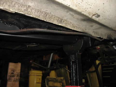 1978 Ford Mustang II - The undercarriage of a vehicle is supported by jack stands, revealing frame components and protective conduit.
