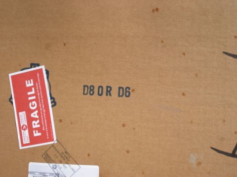 1979 Ford F-150 - A cardboard box with a "FRAGILE" sticker and various shipping labels, indicating it is being transported.