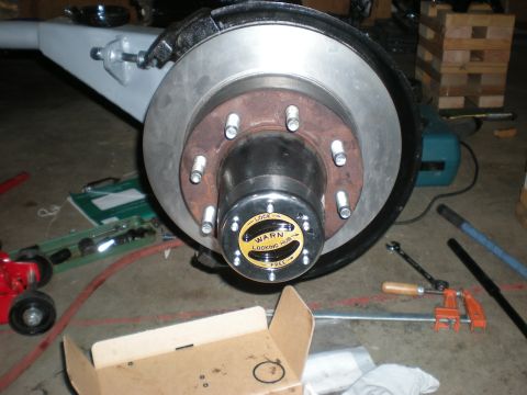 1993 Ford Bronco - A vehicle's front axle assembly with a Warn locking hub is shown, surrounded by tools and repair equipment.