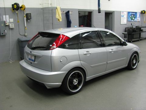 2003 Ford Focus - A silver hatchback with aftermarket black rims is parked inside a garage.