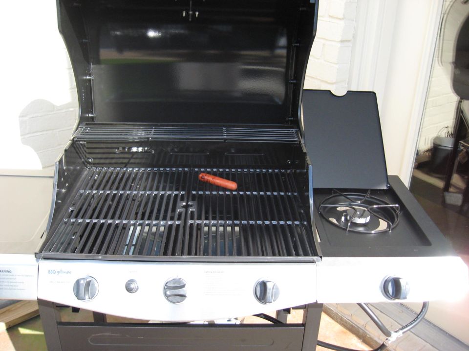 Gas grill with one hot dog on the grates and a side burner