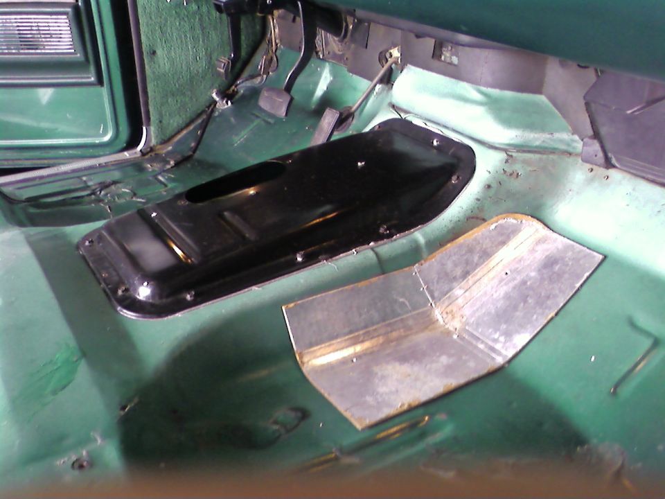 Green vehicle interior floor with black transmission tunnel cover and metal patch